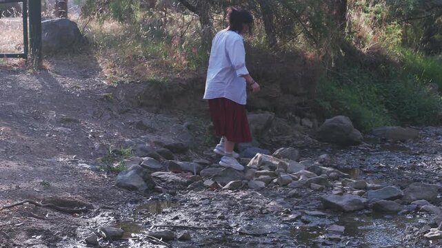 A side angle shot of a girl crossing stones at Warrandyte Park stream. The soft evening sun illuminates the natural setting in Melbourne, capturing the peaceful, rustic atmosphere.