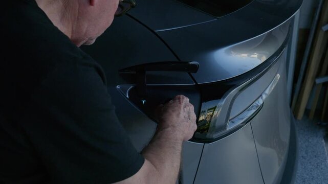 adult senior male opening the hatch on an EV and inserting the charging cable