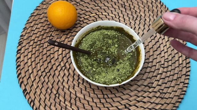Female hands add essential oils with dropper into henna and basma mixture for hair dye preparation closeup