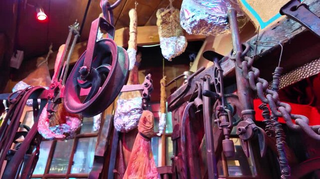 Interior display of traditional charcuterie workshop with hanging cured raw ham, sausage, mechanical pulley and vintage food processing equipment.