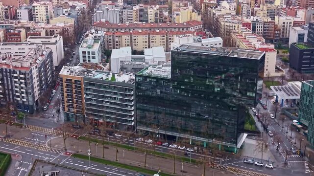 Drone push in along Avinguda Diagonal followed by camera tilt up revealing the Barcelona skyline, modern glass office buildings and dense Eixample district urban cityscape in Catalonia Spain.