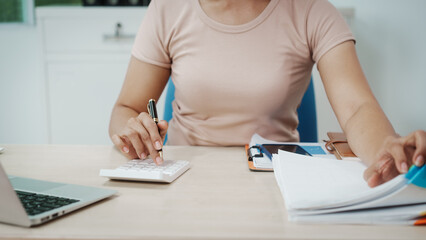 A person using a calculator and organizing papers at a desk, close-up of hands and torso