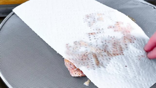 Cook preparing meat for a meal. Close up of a hand using a paper towel to pat dry a seasoned pork chop, removing excess moisture