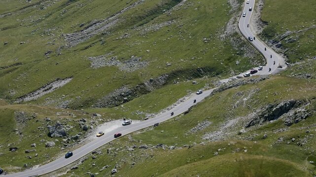 Wide pan right and upward along Transalpina road with cars driving through mountains