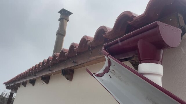 Horizontal video of a broken rain gutter system failing during a storm. Water leaks onto wooden rafters due to a snapped pipe and faulty brackets, showing structural risk. High quality 4k footage