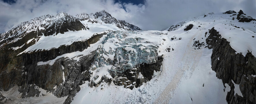Panoramic aerial view of the Argentiere Glacier cascading down rugged, snow-dusted slopes, contrasting with the stark grey rock faces, Chamonix, Auvergne-Rhone-Alpes, France.