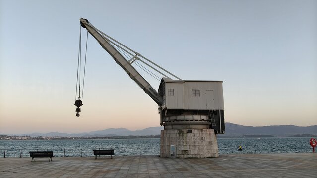 Antigua gr&uacute;a portuaria de carga frente al mar en un muelle al atardecer.