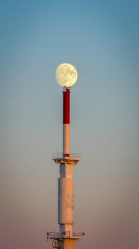 Aerial view of the moon perched atop a white and red tower against a gradient sky, Col de la Faucille, Auvergne-Rhone-Alpes, France.