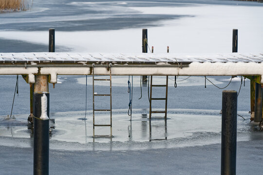Snow covered wooden dock with ladders over frozen icy lake in winter