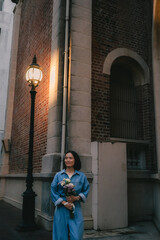 Fototapeta premium Joyful brunette curly woman in trendy pants and shirt smiles in jeans with a bouquet of flowers