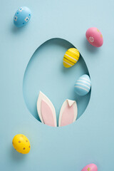 Fototapeta premium Playful vertical pastel Easter eggs and bunny ears peek through a paper cutout creating a cheerful scene for a happy Easter celebration and greeting