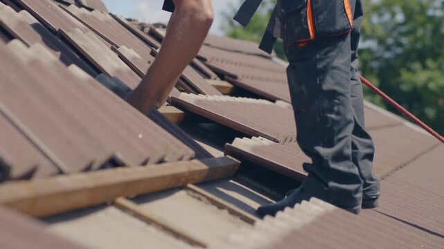 Professional roofer installing ceramic tiles on residential house roof using traditional craftsmanship techniques