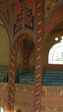 Vertical cinematic interior of historic synagogue with ornate pillar and balcony seating
