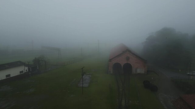 Atmospheric aerial footage of thick fog enveloping rural village buildings and green fields in Paranapiacaba, S&atilde;o Paulo. Moody landscape with misty weather conditions and traditional architecture.