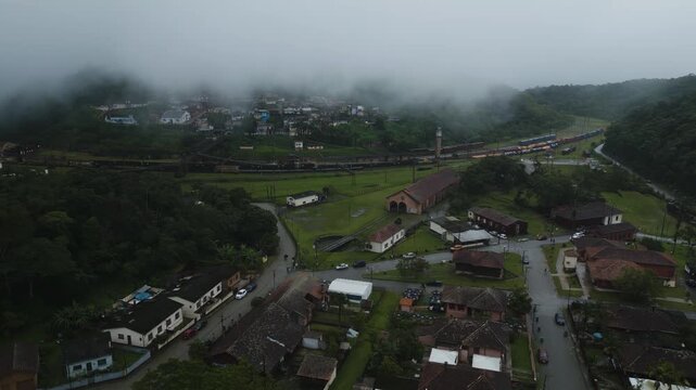 Drone footage of historic Paranapiacaba village in Santo Andr&eacute;, S&atilde;o Paulo, Brazil. Misty mountain settlement with traditional houses, winding roads, and lush green valleys shrouded in atmospheric fog.