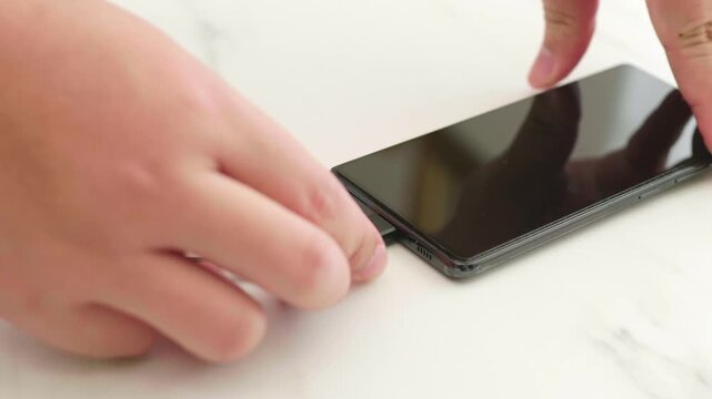 Person hand plugging in usb type c charging cable to modern smartphone on white marble table