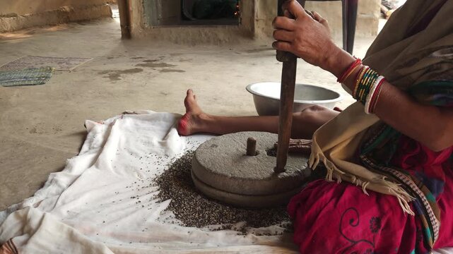 Close-up of a Indian woman using a traditional stone grinder to process grains or spices by hand. This authentic rural scene highlights Indian culture, handmade food preparation