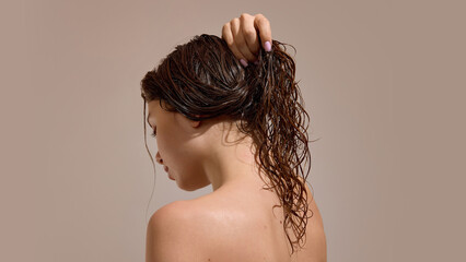 Woman holding wet curly hair in ponytail after washing. Concept of hair handling, moisture control,...