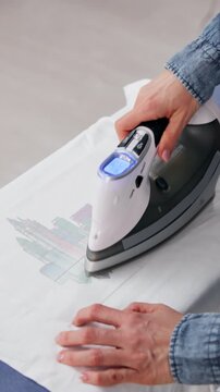 Woman Using Iron-On Heat Transfer To Apply Custom Design On T-Shirt
