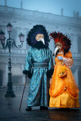 Obraz premium Venice, Italy - February 13, 2026: Two masked figures in elaborate costumes stand in a foggy square during the Venice Carnival, showcasing vibrant colors and intricate details