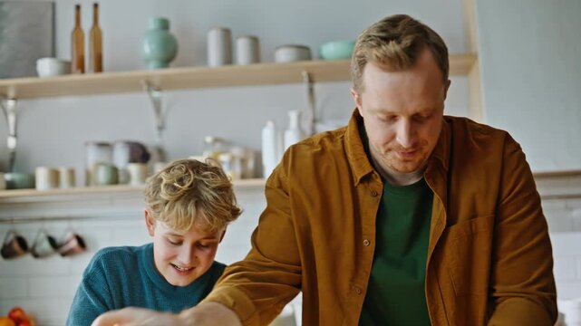 Father son hands kneading dough adding flour on kitchen countertop closeup.