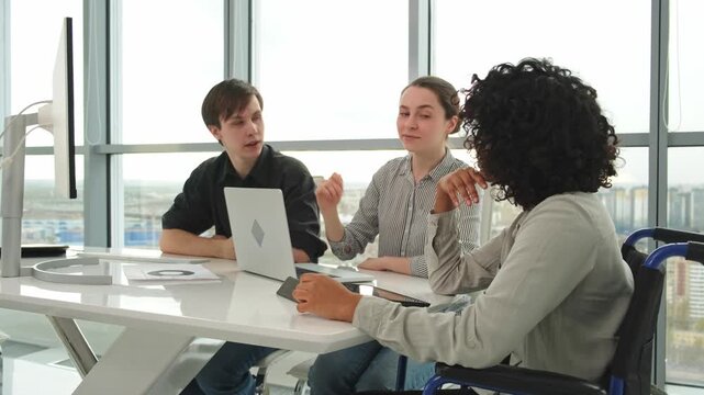 Teamwork brainstorm. Diverse multiracial colleagues woman in chair for people with disability working together. Group of people sitting in creative office discussing business. Young professional team
