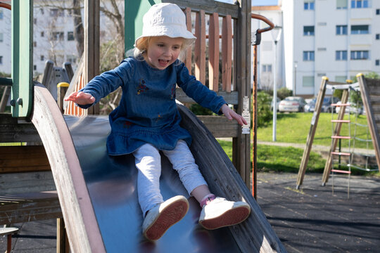 Happy 4 year old girl sliding down a slide at the playground