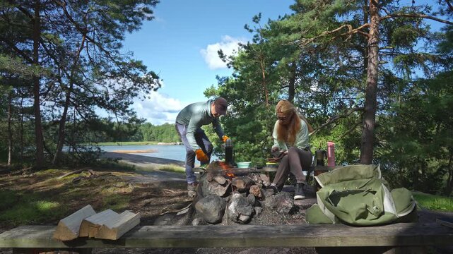 Young couple preparing meal in Finnish national park protected area. Sustainable eco-tourism and nature conservation concept with authentic lifestyle and mental wellness in sunny forest.