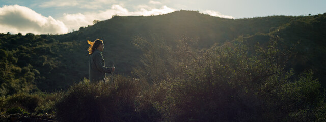 Backlit brunette woman, hair in the wind, stands on a hill in countryside. Malaga, Andalusia, Spain. © ysbrandcosijn