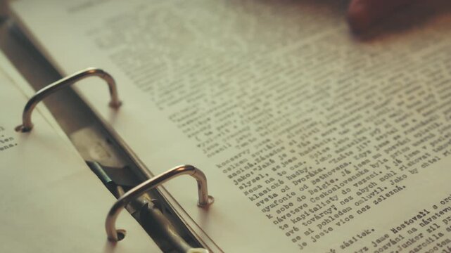 Close-up of a hand smoothing a typewritten page into a loose-leaf binder before closing the cover. Captures tactile archival research and organization.