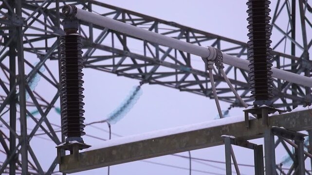 Close view of snow covered substation hardware with icy insulators cables and steel structures during a freezing winter day.