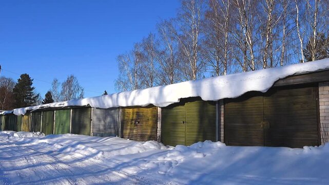 Slow pan across old garage boxes with colorful doors deep snow and leafless birch trees glowing in cold winter sunlight.