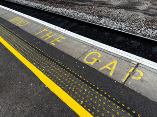 Mind the gap painted on train platform edge at York UK station with yellow safety line and tactile paving