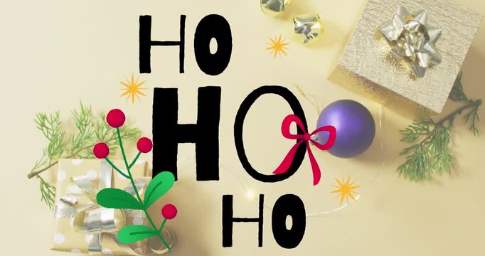 Animation of ho text banner over christmas gifts and decorations on yellow surface