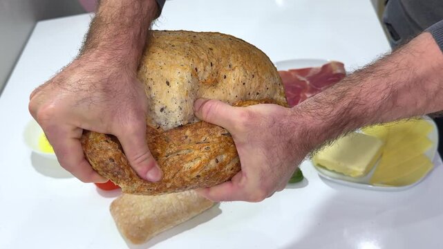 Breaking rustic bread Slow motion of hands breaking a freshly baked loaf of bread