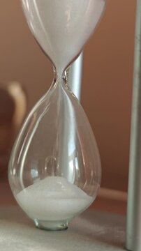 Glass hourglass with flowing white sand, showcasing the continuous passage of time as grains shift from the upper to the lower chamber in a softly lit environment