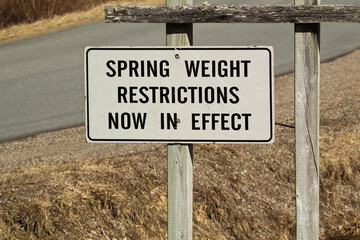 Roadside sign indicating spring weight restrictions in effect along a quiet rural road during early thaw season. © Kevin Brine