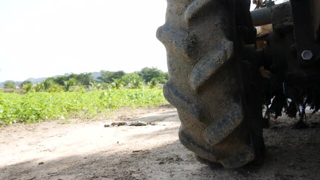 Small agricultural tractor stands on a dirt road with open field grass and sky forming a rural working environment. Farm machinery.