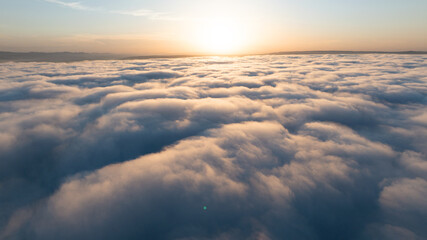 Aerial landscape sunset above clouds bright sun. Thick cloud layer drone shot high altitude. Scenic...