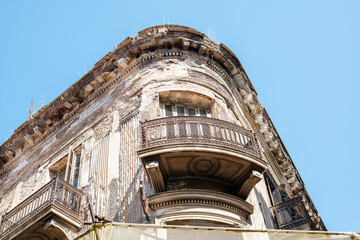 Detailed view of a vintage apartment building corner with traditional metal balconies. Textured aged walls of a historical property against a vibrant blue sky. European city heritage and architecture. © marina_larina