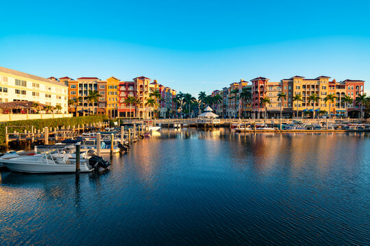 Colorful Mediterranean style buildings line the waterfront of a calm marina in Naples, Florida.