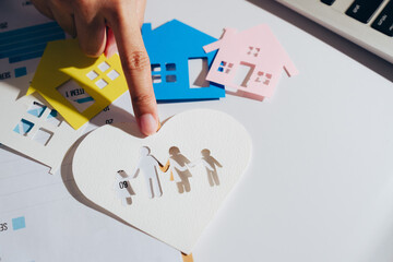Paper cutouts of houses in various colors surround heart shaped cutout depicting family holding...
