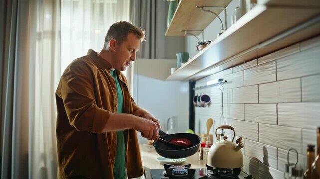 Guy turning over meat on frying pan using spatula home closeup. Man cooking