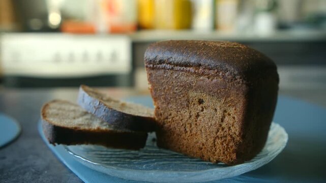Delicious half loaf of dark rye bread with two cut slices resting on clear glass plate in kitchen, showcasing fresh, porous texture nutritious whole grain food. Freshly baked sliced rye bread on plate