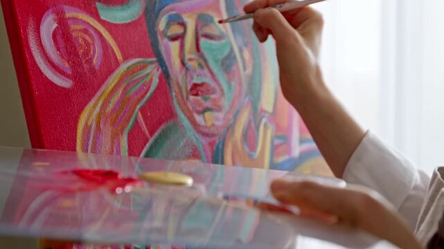 Artist hand painting expressive male portrait on canvas with brush and palette.