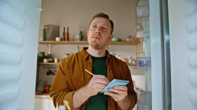 Guy making shopping list looking empty refrigerator home kitchen closeup pov