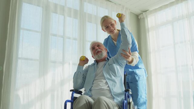 Support rehabilitation healthcare. Nurse helps old man patient in wheelchair picking up dumbbells. Paralyzed man in chair for people with disability doing sports exercise with nurse. Medical caregiver