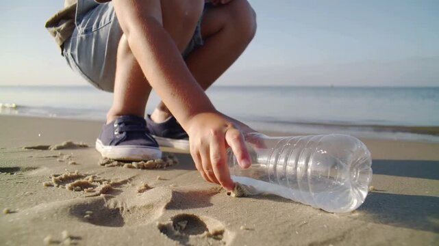 Bottle plastic being picked up on sandy beach with ocean in background and person wearing shorts and shoes featuring cleanup, litter, pollution