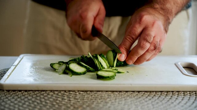 Slicing cucumbers at kitchen table in simple steps during afternoon hours for fresh salad