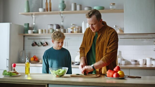 Father slicing vegetable teaching son cooking food standing kitchen closeup.